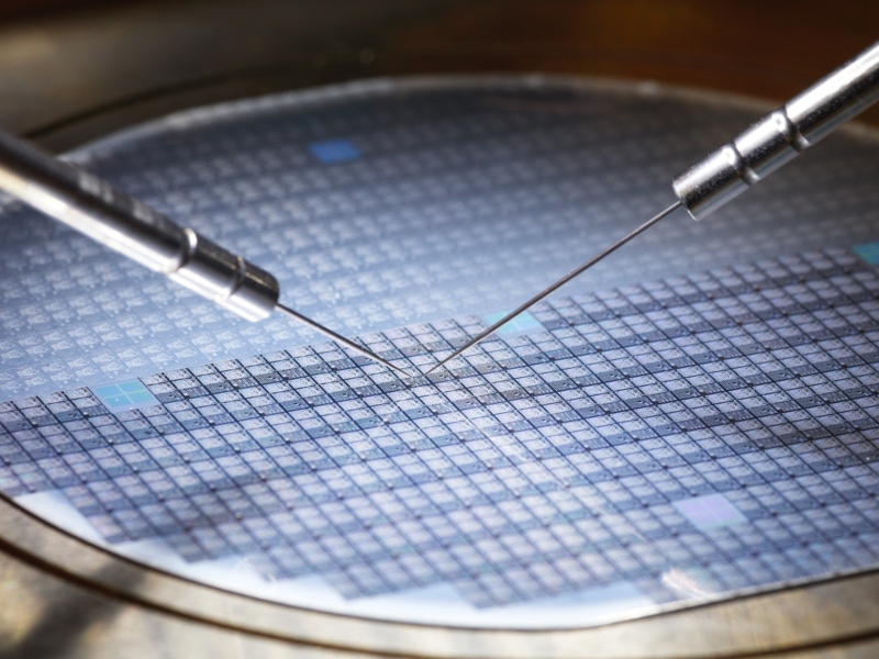 Probe needles contacting a patterned semiconductor wafer during electrical testing.